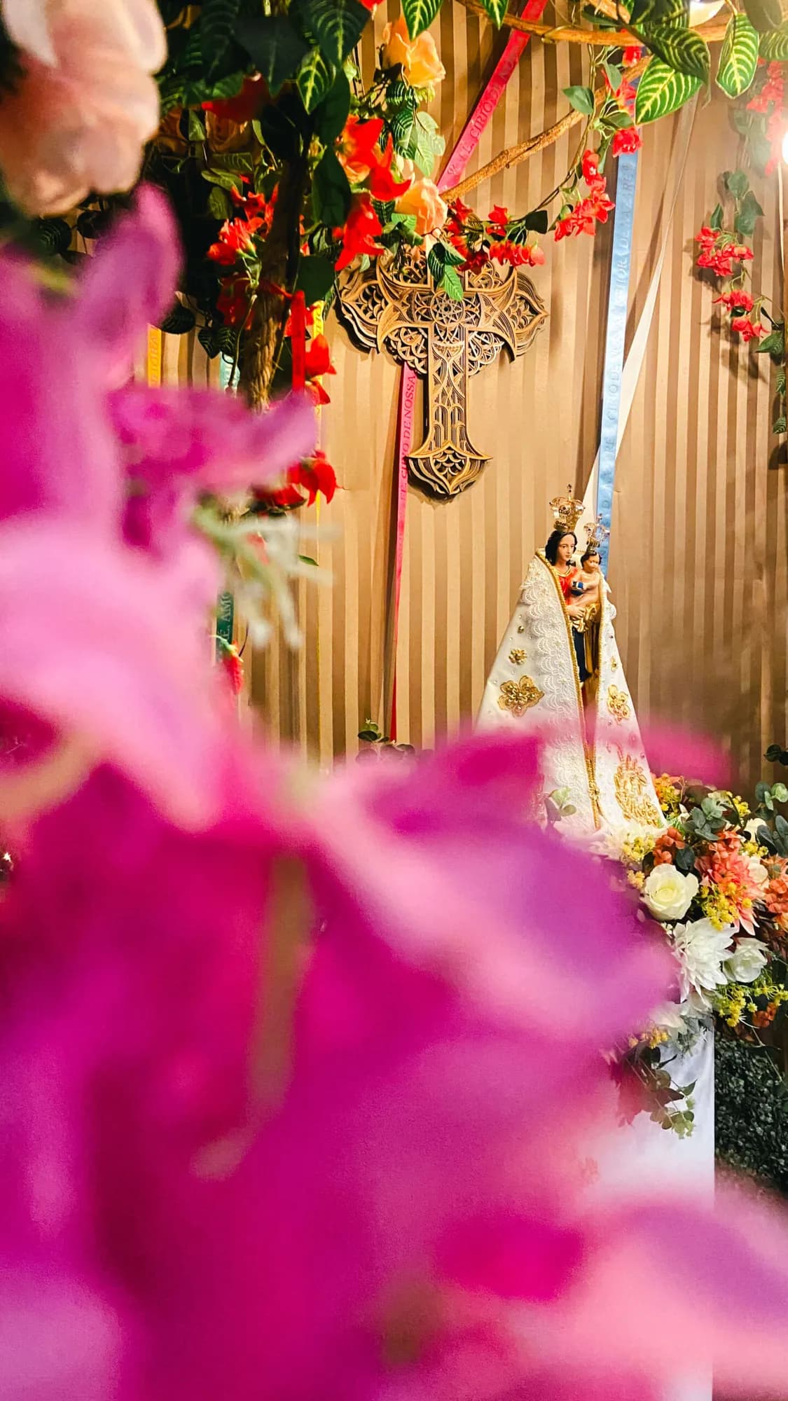 Flores rosa em primeiro plano diante de altar decorado para festa religiosa